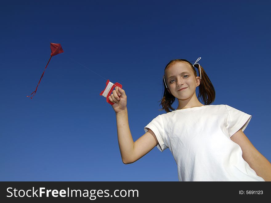 Girl wearing white shirt flying a kite with blue sky