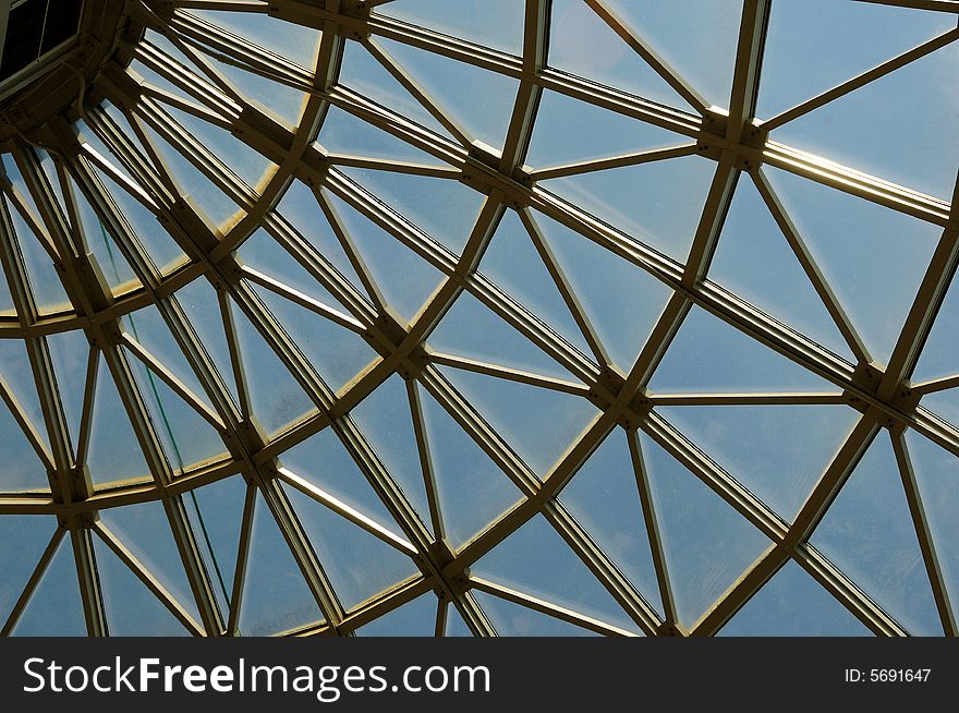 Silver metal curved roof joists in a conservatory with glass panes in between and a blue sky. Silver metal curved roof joists in a conservatory with glass panes in between and a blue sky