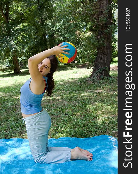 A girl, on a blue towel in the middle of the park, doing some exercises with a ball. A girl, on a blue towel in the middle of the park, doing some exercises with a ball