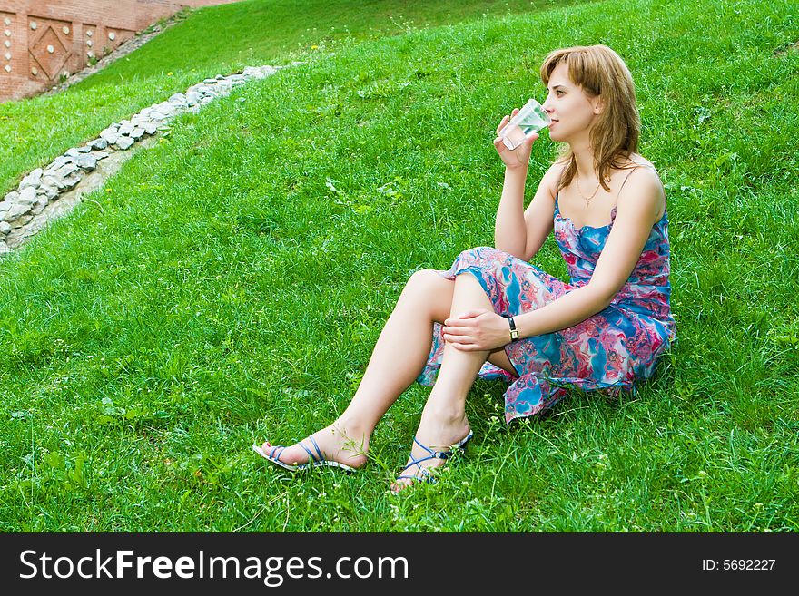 Girl drinks water from a glass sitting on a green grass. Girl drinks water from a glass sitting on a green grass