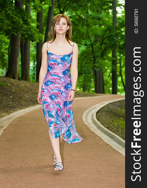 Beautiful young girl in a summer dress goes on a path in park. Beautiful young girl in a summer dress goes on a path in park