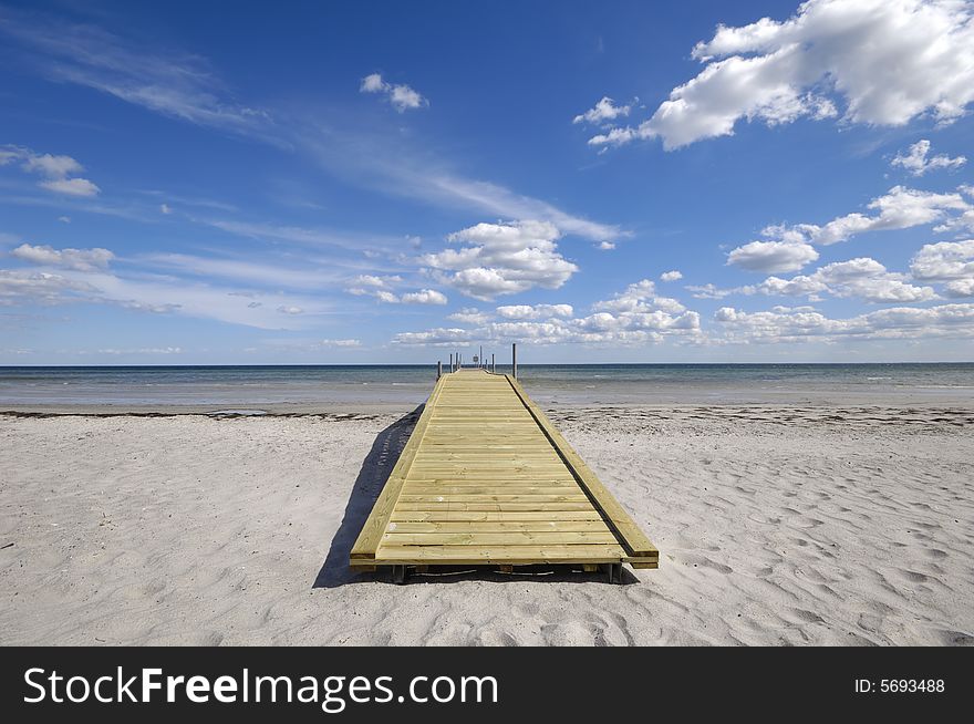 Bridge on beach. The sky is blue with cluds.