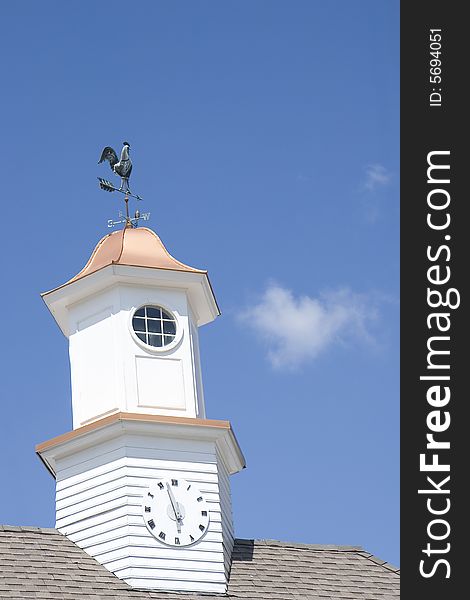 A clock and a weathervane on a cupola against blue sky. A clock and a weathervane on a cupola against blue sky