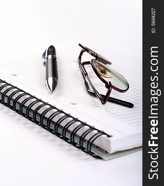 Notepad with eyeglasses and pen isolated on white