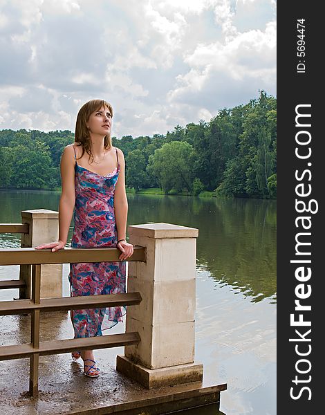 Attractive girl stands on quay on a background of wood lake