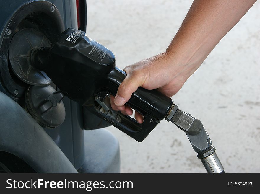 Close up of a man's hand pumping gas into a blue vehicle. Close up of a man's hand pumping gas into a blue vehicle.