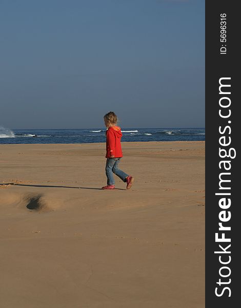 A white caucasian little girl walking alone on the beach. A white caucasian little girl walking alone on the beach