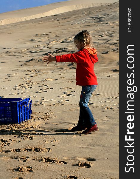 A beautiful white caucasian girl child playing with a blue container on the beach. A beautiful white caucasian girl child playing with a blue container on the beach