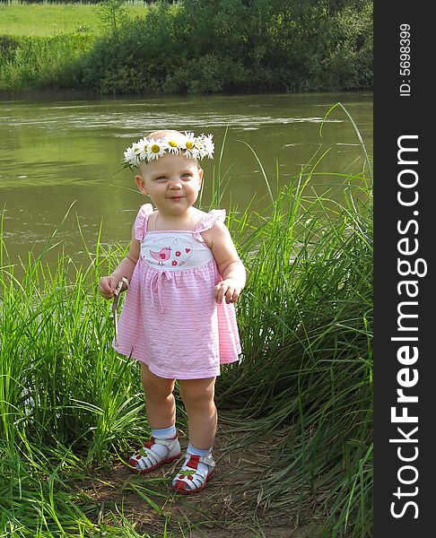 Little girl with camomiles garland beside river. Little girl with camomiles garland beside river