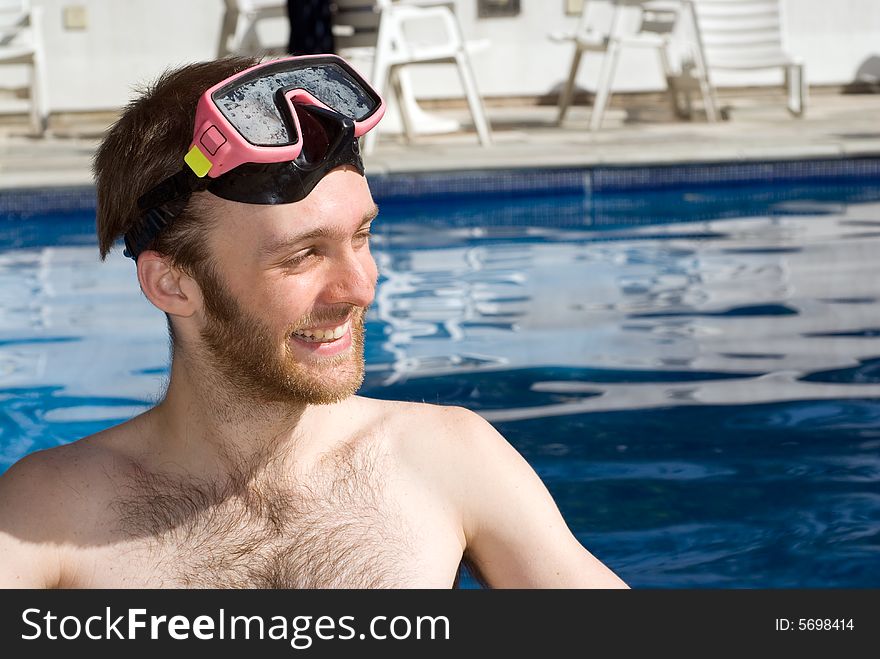 A Man is standing in a pool. He is smiling and looking away from the camera. He is wearing goggles. Horizontally framed photo. A Man is standing in a pool. He is smiling and looking away from the camera. He is wearing goggles. Horizontally framed photo.