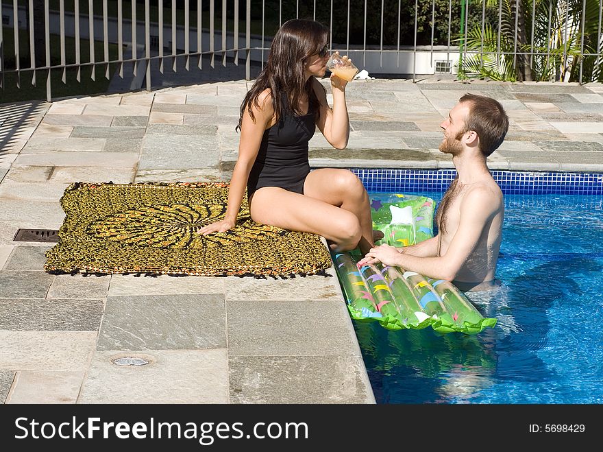 A young, attractive couple are beside the pool, staring and drinking. - horizontally framed. A young, attractive couple are beside the pool, staring and drinking. - horizontally framed