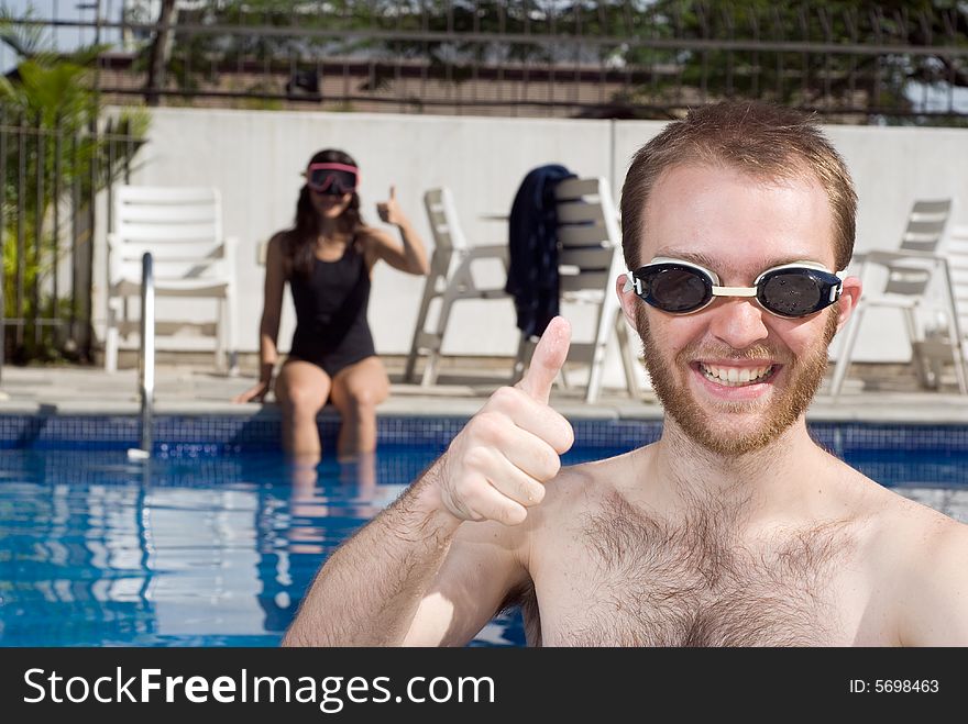 A man and a woman are sitting in a pool giving thumbs up signs.  The woman is on the far end of the pool looking at the camera.  The man is standing right in front of the camera looking at it.  Horizontally framed photo. A man and a woman are sitting in a pool giving thumbs up signs.  The woman is on the far end of the pool looking at the camera.  The man is standing right in front of the camera looking at it.  Horizontally framed photo.