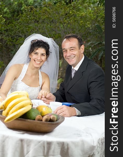 A newly married couple, at a table with fruits on it, smile for the camera together. - vertically framed. A newly married couple, at a table with fruits on it, smile for the camera together. - vertically framed