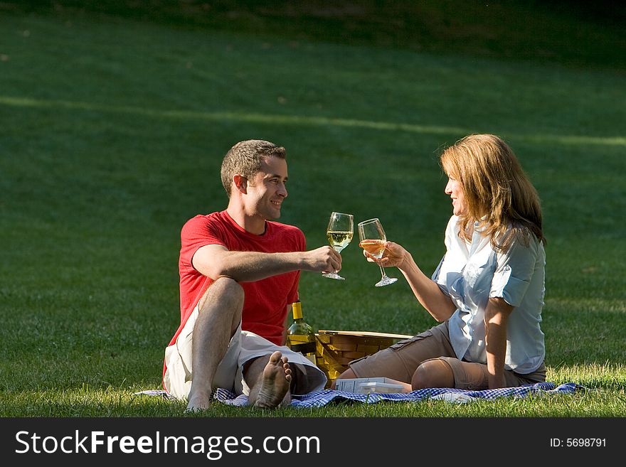 A couple, sitting down, drink together in a park. - horizontally framed. A couple, sitting down, drink together in a park. - horizontally framed