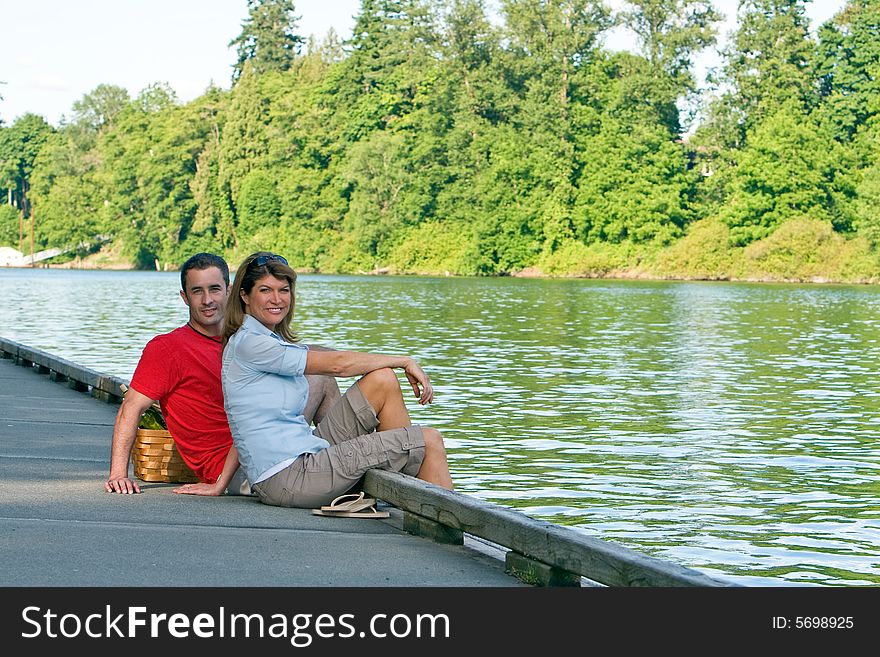 A young couple, sit on a lake dock, together. - horizontally framed. A young couple, sit on a lake dock, together. - horizontally framed