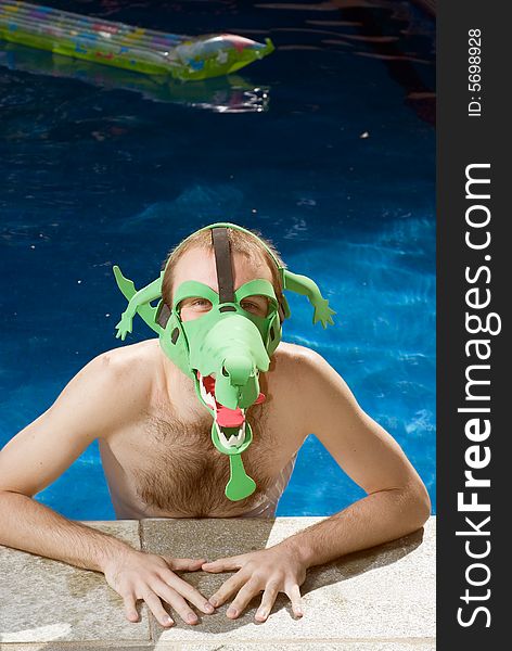 A man, in the pool, looks at the camera while wearing a funny, green crocodile mask. - vertically framed. A man, in the pool, looks at the camera while wearing a funny, green crocodile mask. - vertically framed