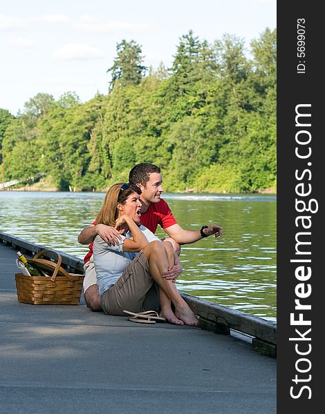 A young couple, sit together on the dock looking at the scenery. - vertically framed. A young couple, sit together on the dock looking at the scenery. - vertically framed