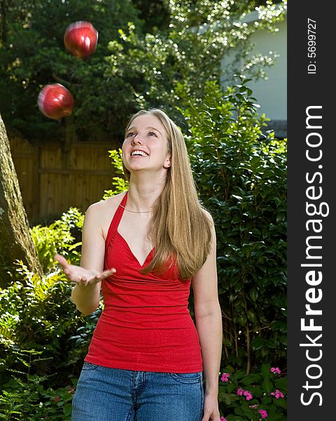 Pretty blond young woman/teenager juggling two apples outdoors. Pretty blond young woman/teenager juggling two apples outdoors