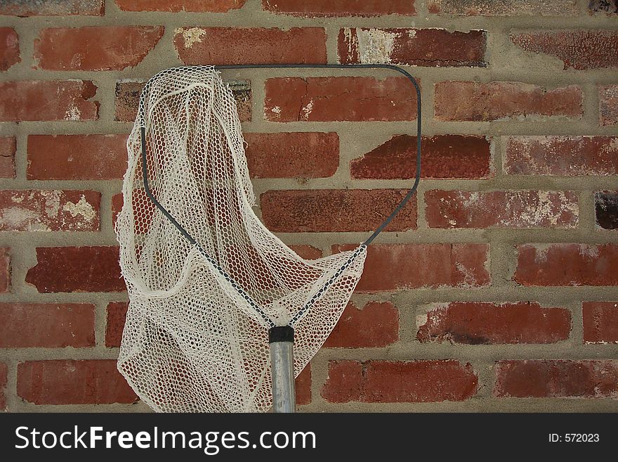 A torn fishing net resting against a brick wall.