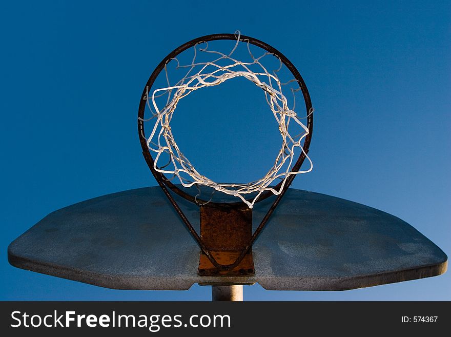 A rusty old basketball hoop against a blue sky in the evening.