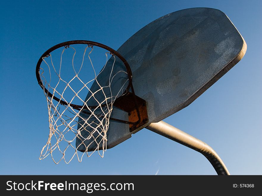 A rusty old basketball hoop against a blue sky in the evening.