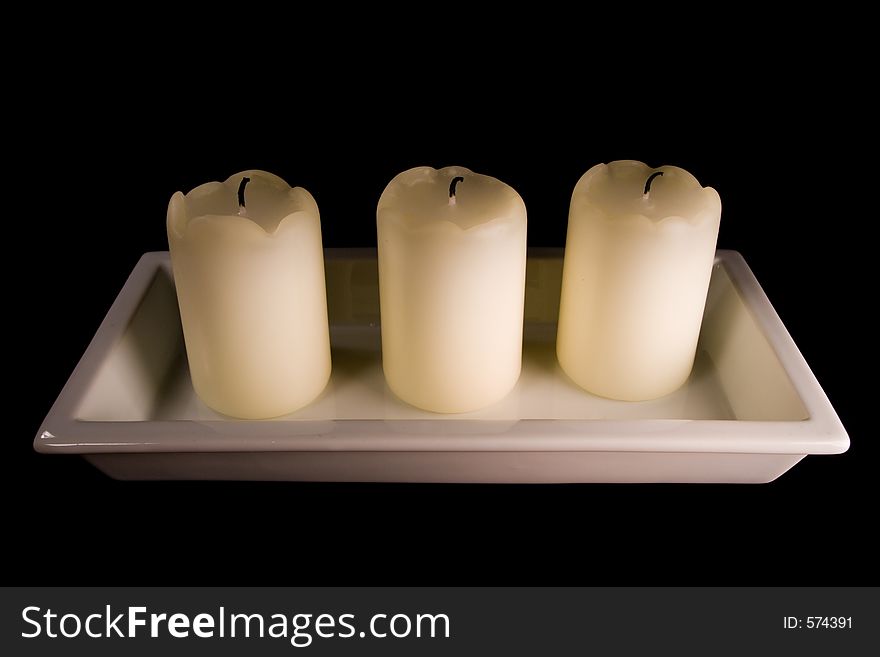 Three white candles lined up in a white saucer isolated on black. Three white candles lined up in a white saucer isolated on black