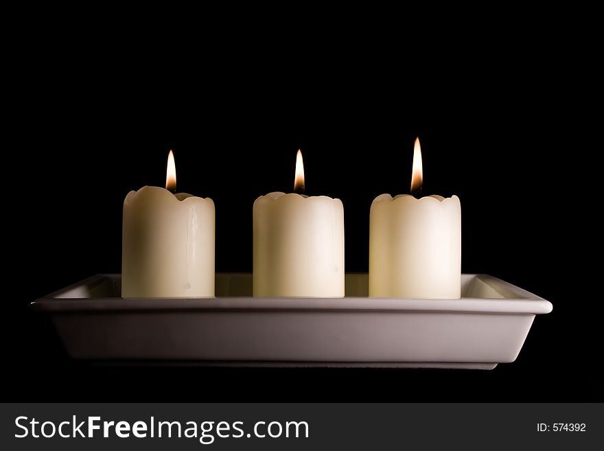 Three white candles lined up in a white saucer isolated on black. Three white candles lined up in a white saucer isolated on black