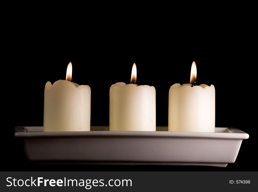 Three white candles lined up in a white saucer isolated on black. Three white candles lined up in a white saucer isolated on black