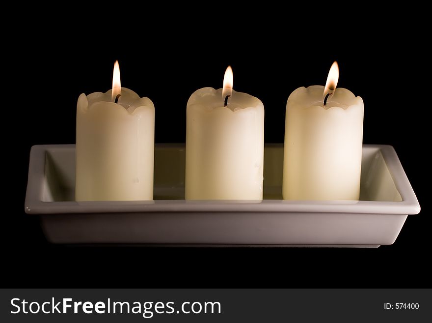 Three white candles lined up in a white saucer isolated on black. Three white candles lined up in a white saucer isolated on black