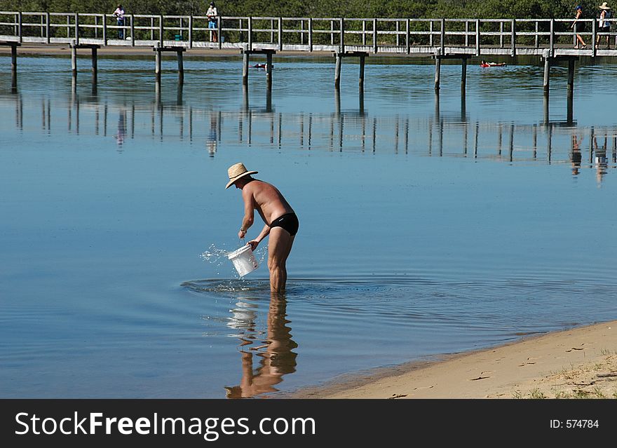 Man filling a bucket with water by the pier