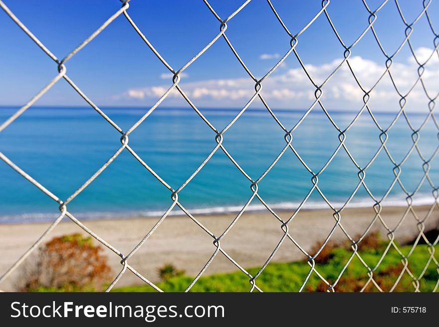 Beautiful paradise beach as seen through teasing wires of a steel fence on a sunny day. Beautiful paradise beach as seen through teasing wires of a steel fence on a sunny day