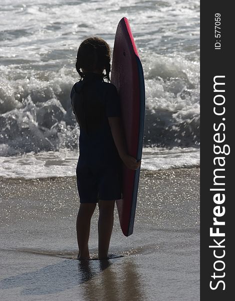 A young girl contemplates the ocean in front of her, as she clutches her boogie board. She is silhouetted by the late afternoon sun. A young girl contemplates the ocean in front of her, as she clutches her boogie board. She is silhouetted by the late afternoon sun.