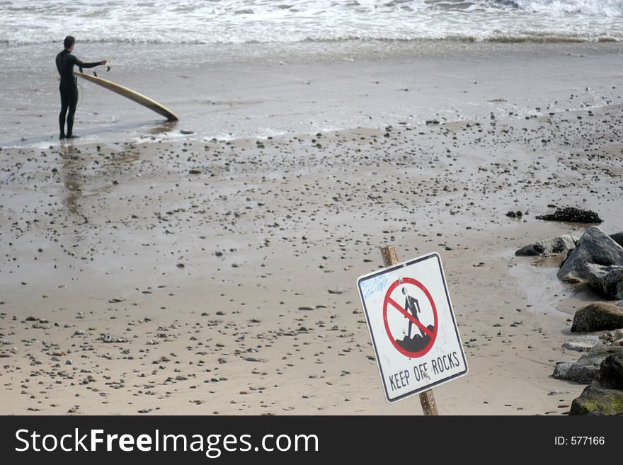 Man preparing to surf, warning sign in the foreground. Man preparing to surf, warning sign in the foreground