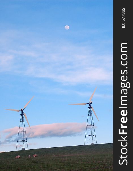 Sheep standing on a hillside with a windmill towering above, with the moon in the sky. Sheep standing on a hillside with a windmill towering above, with the moon in the sky