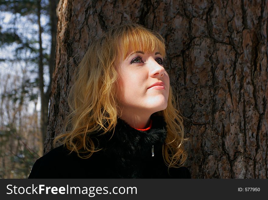 The young beautiful girl in a wood stands near a tree