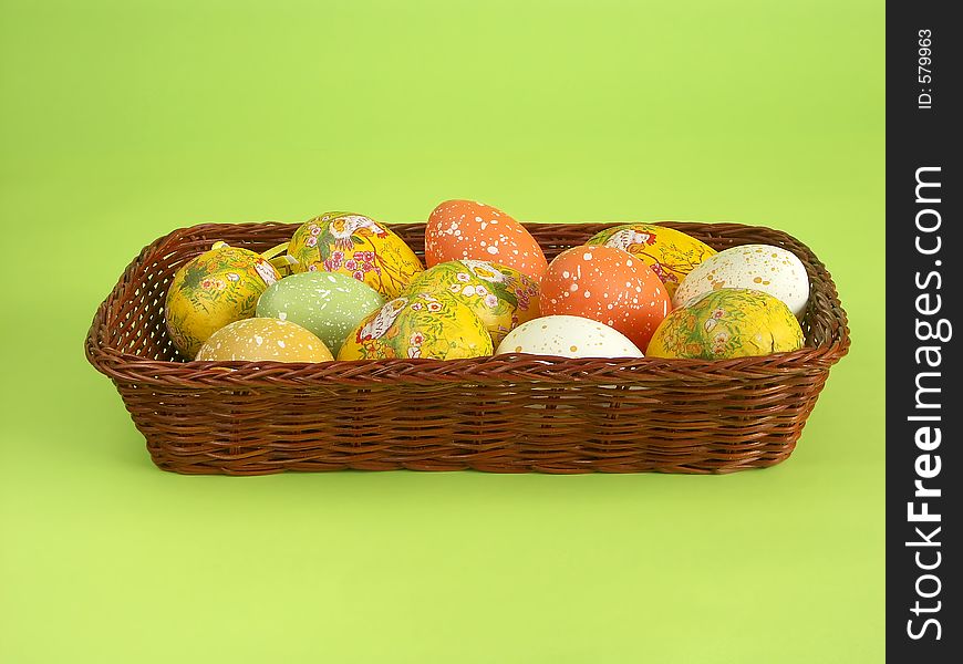 Wicker basket with Easter eggs over light green background. Wicker basket with Easter eggs over light green background
