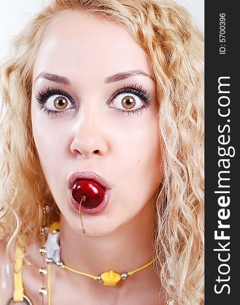 Beauty young woman with opened surprised eyes and red cherry in mouth