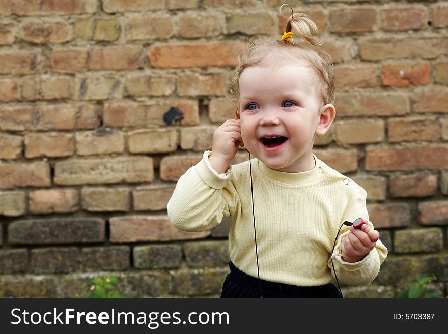 The baby-girl listens to music on a background of a brick wall. The baby-girl listens to music on a background of a brick wall