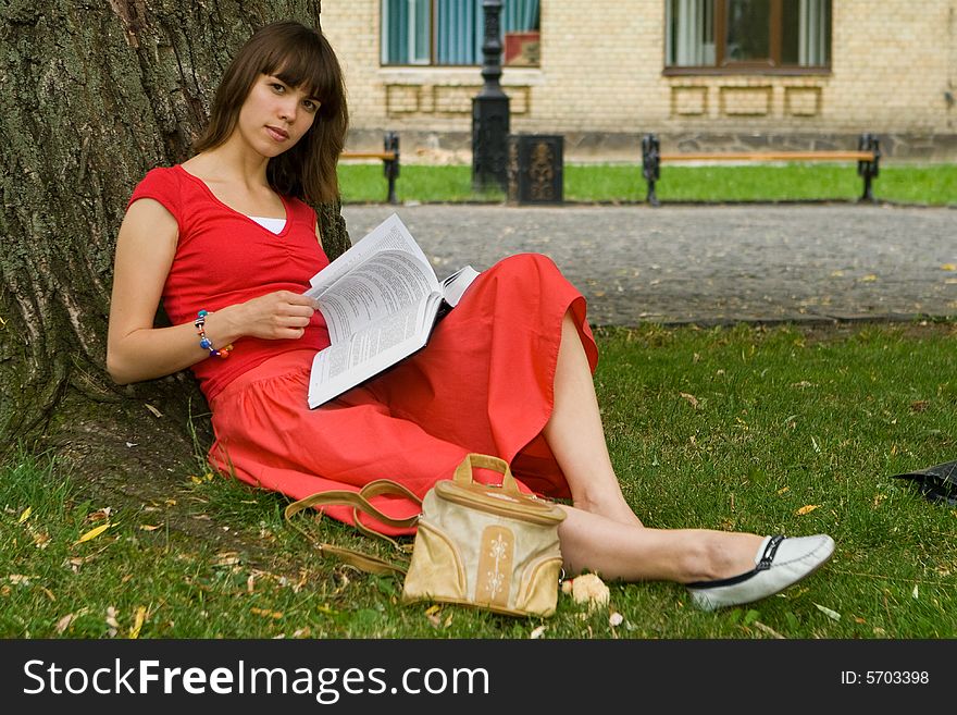 A beautiful young college girl under a tree reading a book. A beautiful young college girl under a tree reading a book