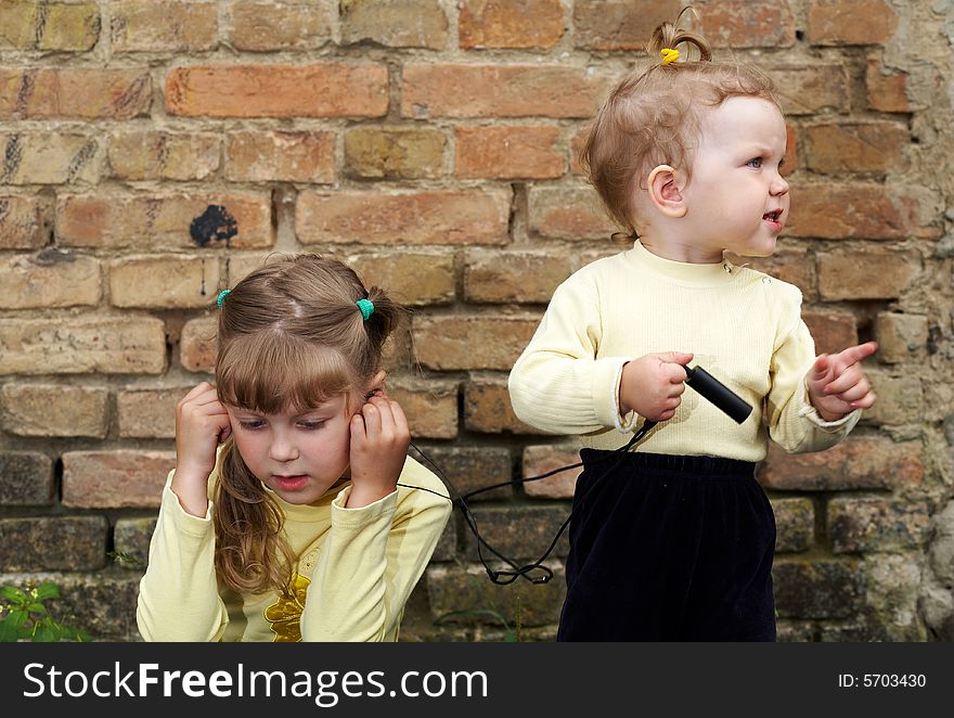 Two little sisters listens to music on a background of a brick wall. Two little sisters listens to music on a background of a brick wall