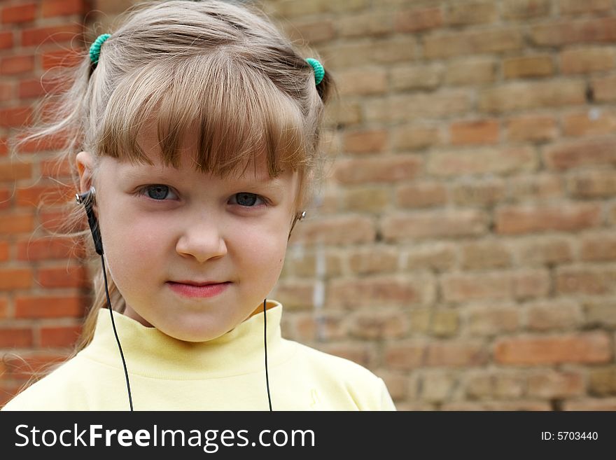 The young nice girl listens to music on a background of a brick wall