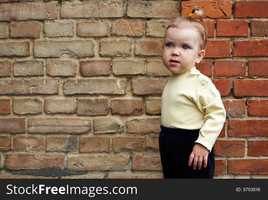 An image of baby-girl near a yellow brick wall