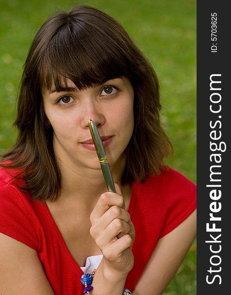 A beautiful young college girl holding a pen near her nose. A beautiful young college girl holding a pen near her nose