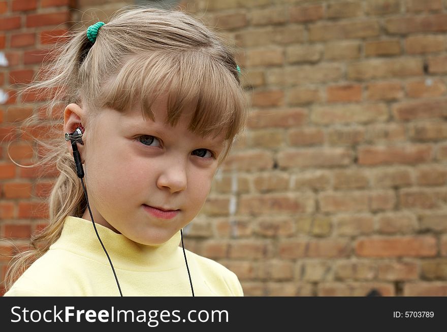 The young girl listens to music on a background of a brick wall. The young girl listens to music on a background of a brick wall