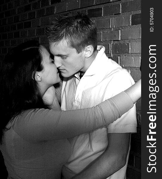 Couple kissing against brick wall, in black and white. Couple kissing against brick wall, in black and white