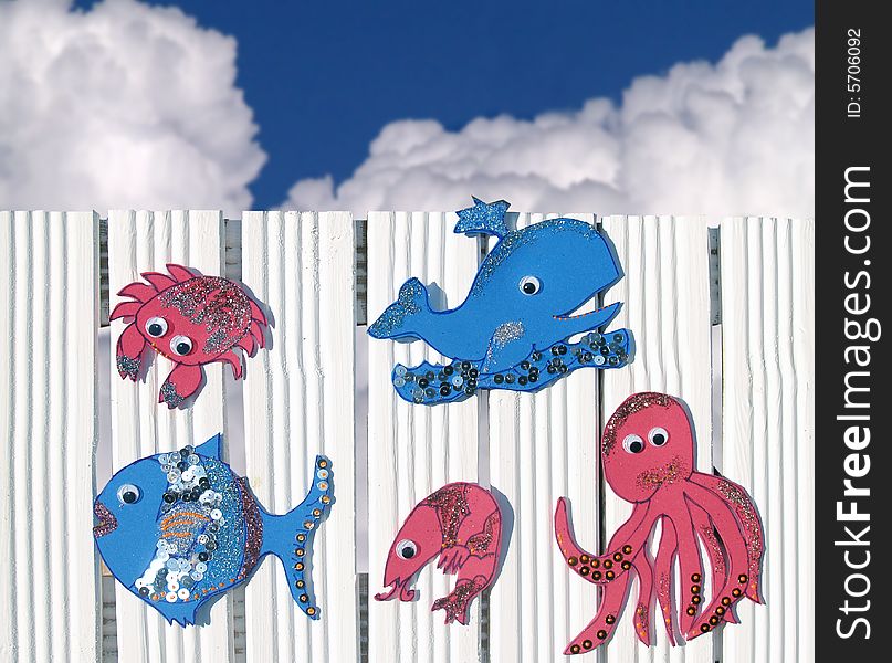 Sea creatures made of moosgummi at white fence, blu sky at background