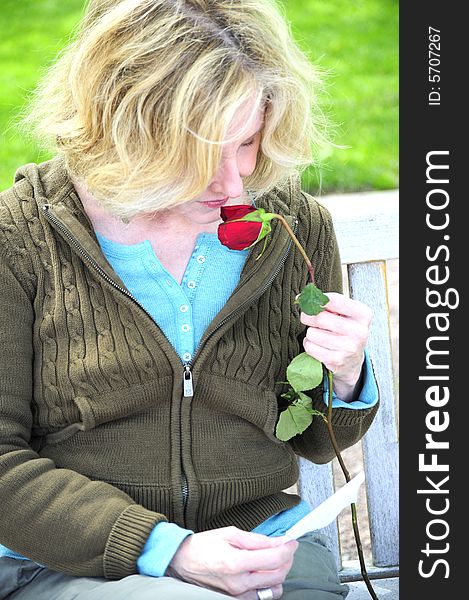 Woman smelling a rose while sitting on a park bench. Woman smelling a rose while sitting on a park bench.