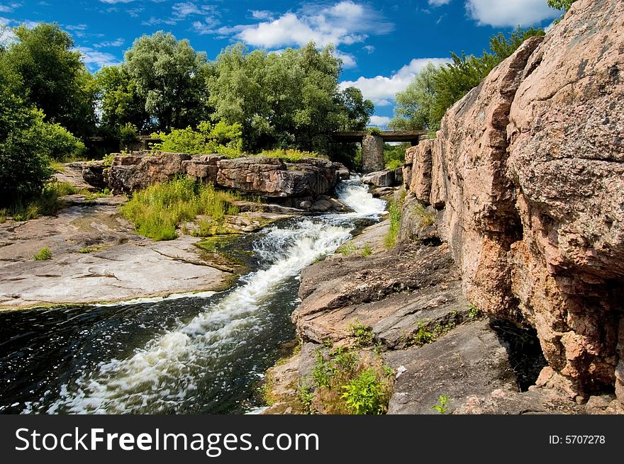 River Stream With Rocks And Bridge