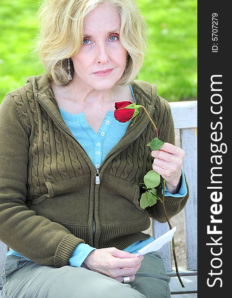 Woman smelling a rose while sitting on a park bench. Woman smelling a rose while sitting on a park bench.