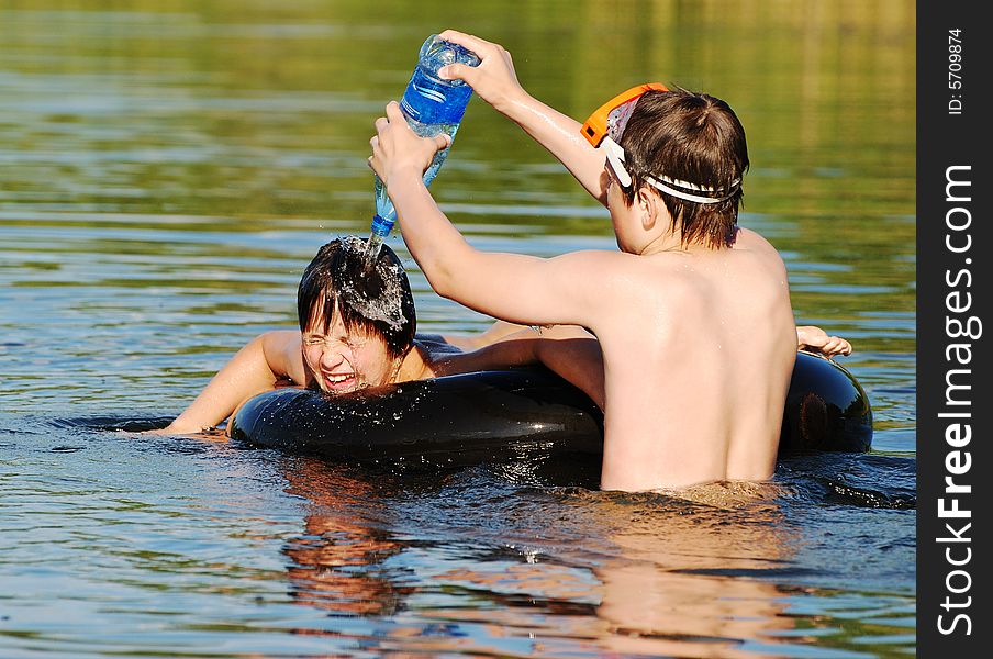The boy pouring water from the plastic bottle onto his friends' head in a small lake late afternoon. The boy pouring water from the plastic bottle onto his friends' head in a small lake late afternoon.